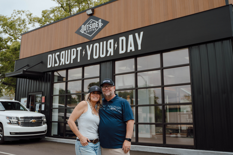 Couple posing outside a restaurant with a “DISHOUT YOUR DAY” sign