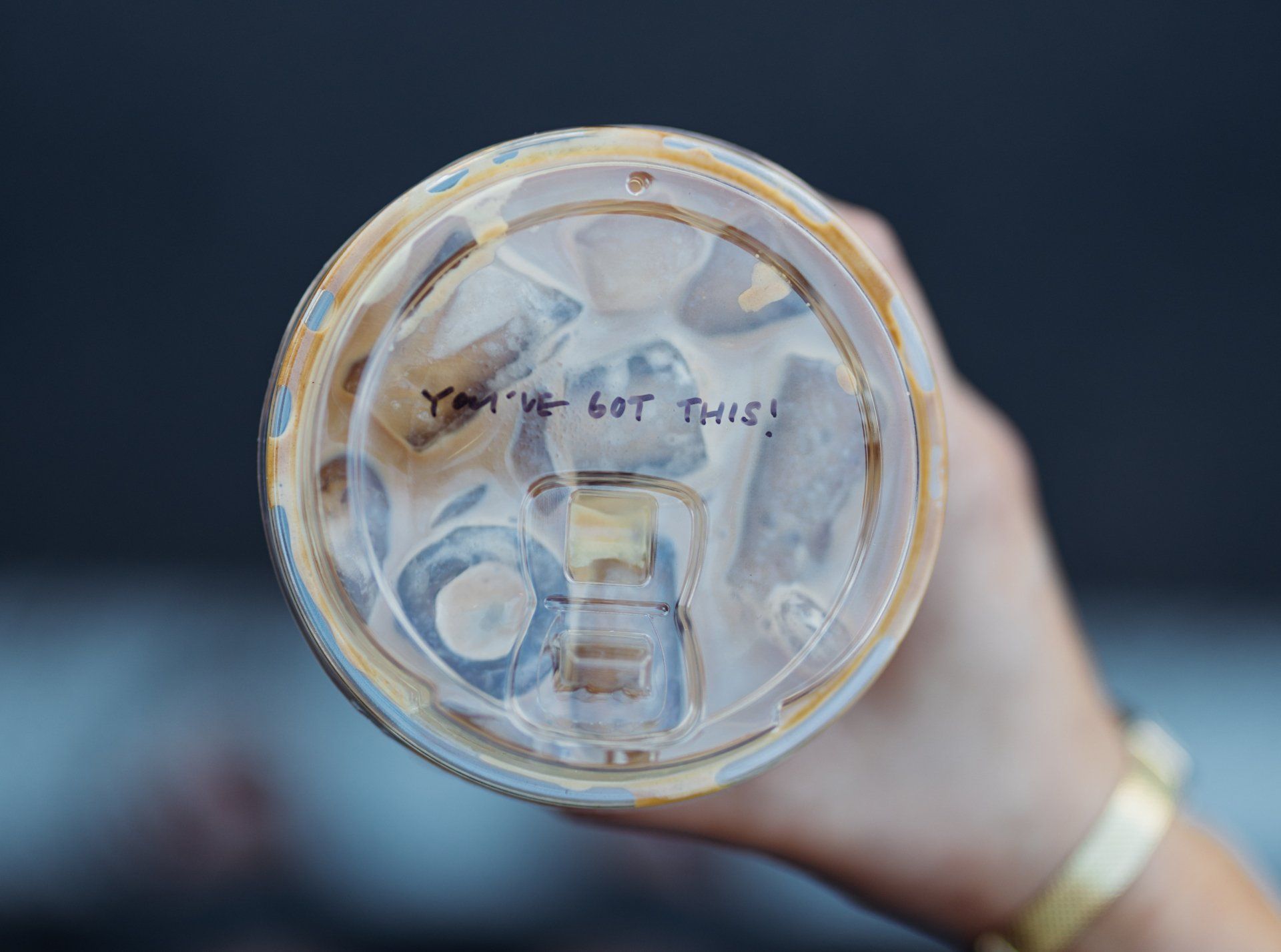 Close-up of a reusable cup lid held up, with a handwritten note visible through the clear top.