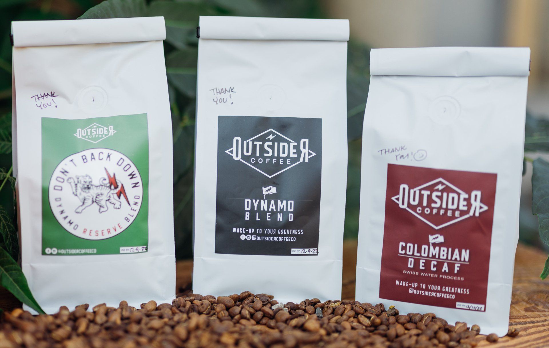 Three white coffee bags with green, gray, and red labels beside spilled coffee beans