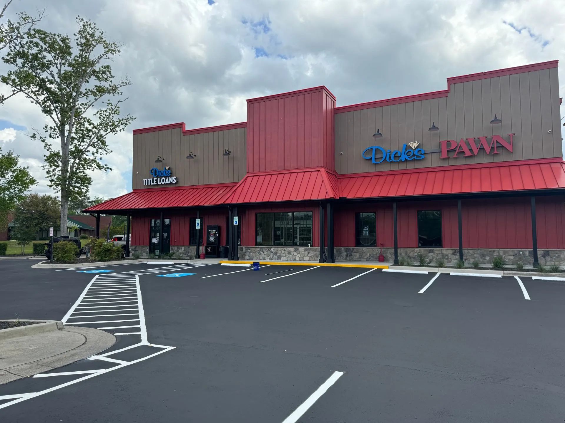 A modern, single-story retail building with red metal roofing, tan metal siding, and stone accents, plus a parking lot.