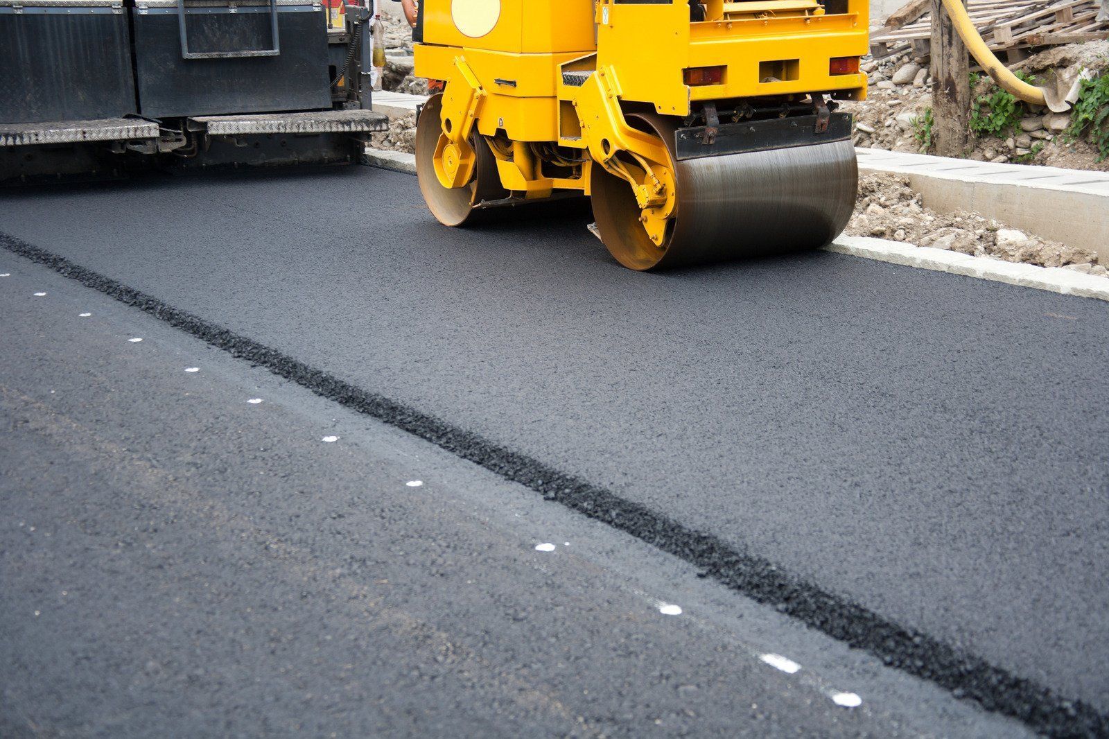 A yellow roller is rolling asphalt on a road.