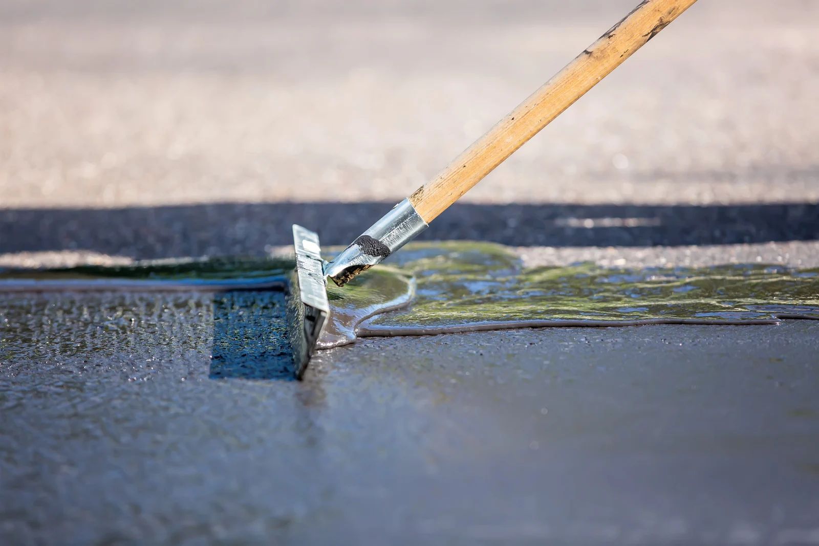 Paint roller spreading gray coating on a wet asphalt surface outdoors