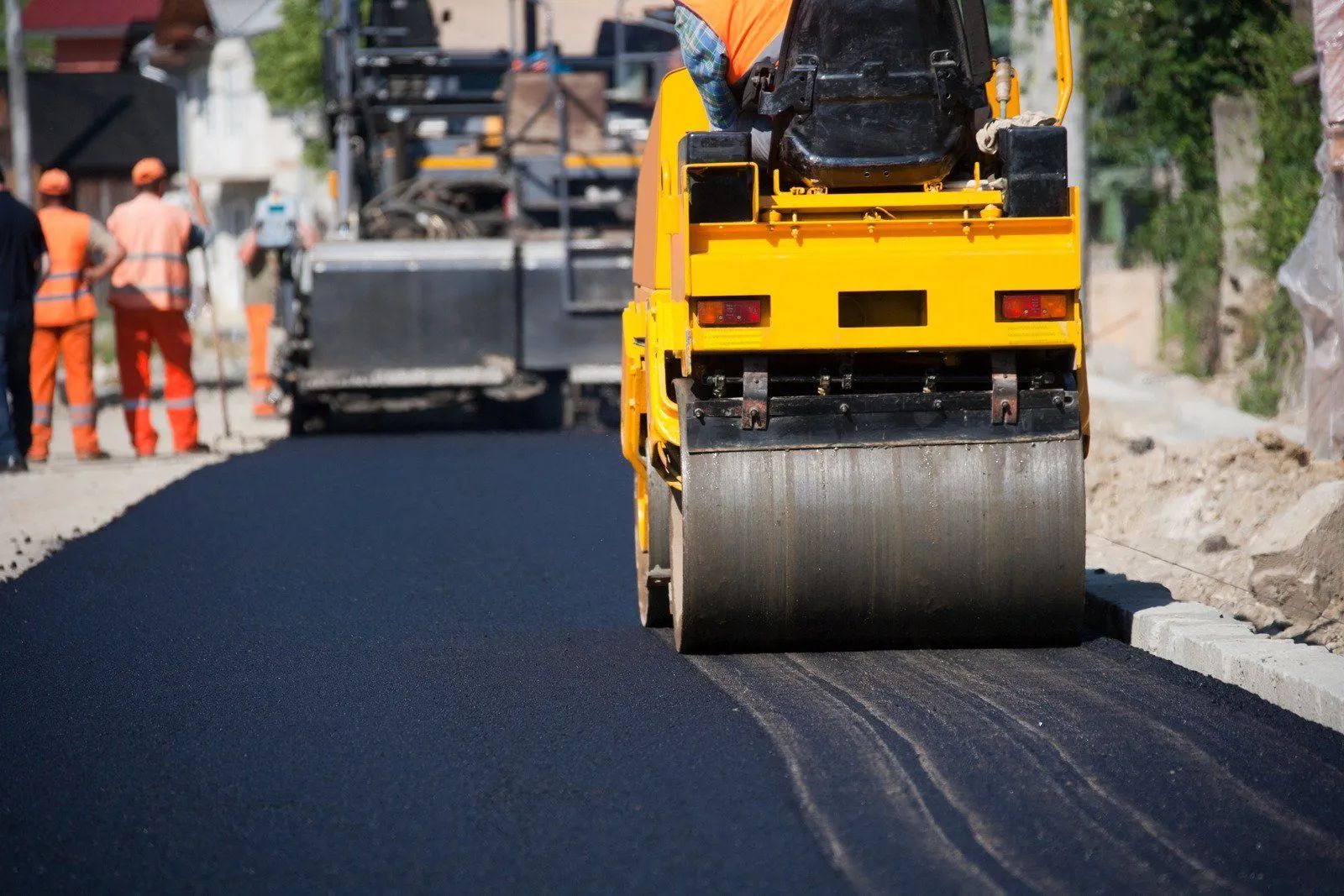 Road roller paving fresh asphalt with workers in the background on a street construction site
