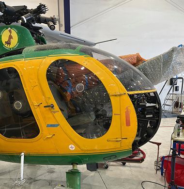 Yellow and green helicopter cockpit inside a hangar, undergoing maintenance.