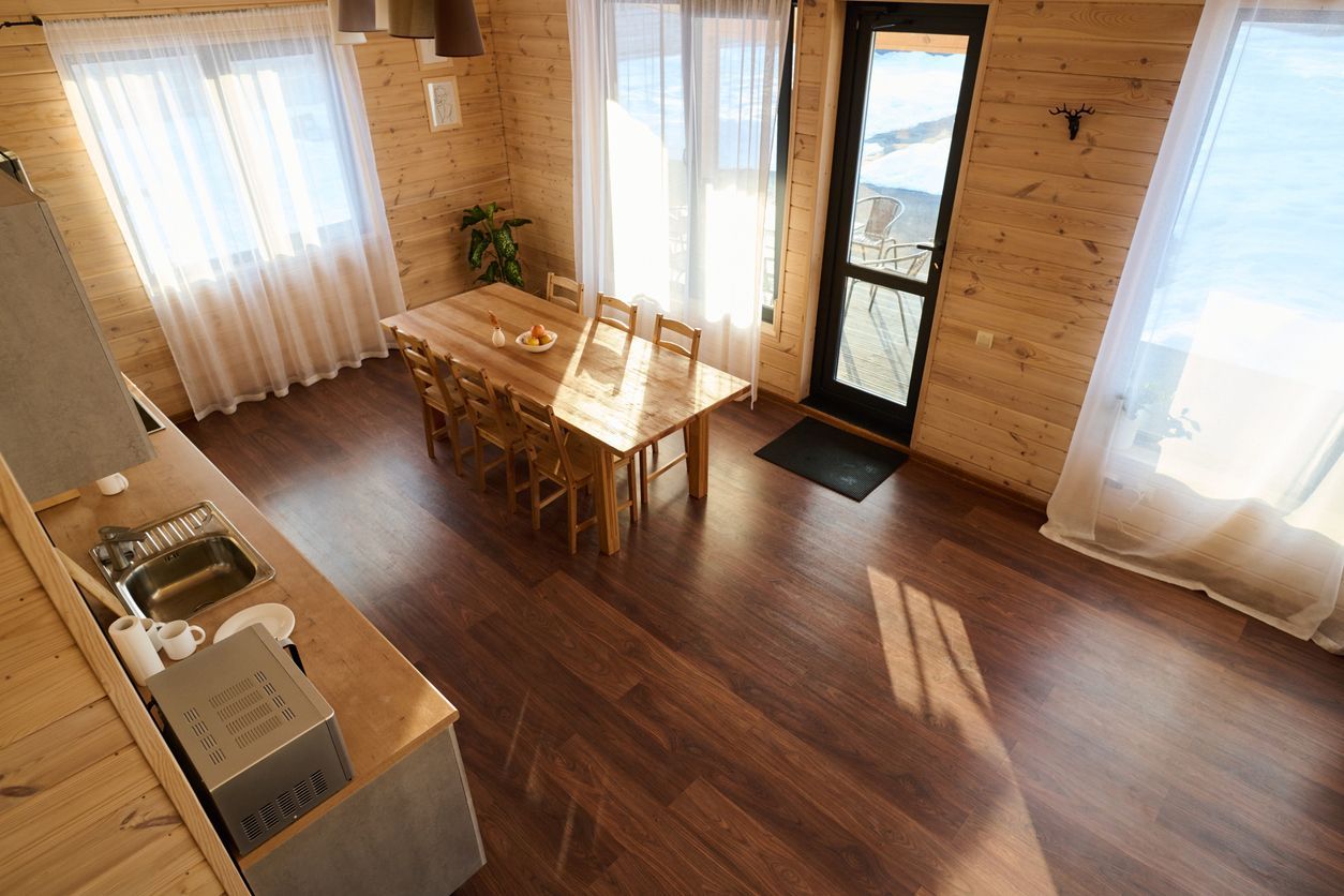 Sunlit wooden dining room with table, chairs, large windows, and a glass door