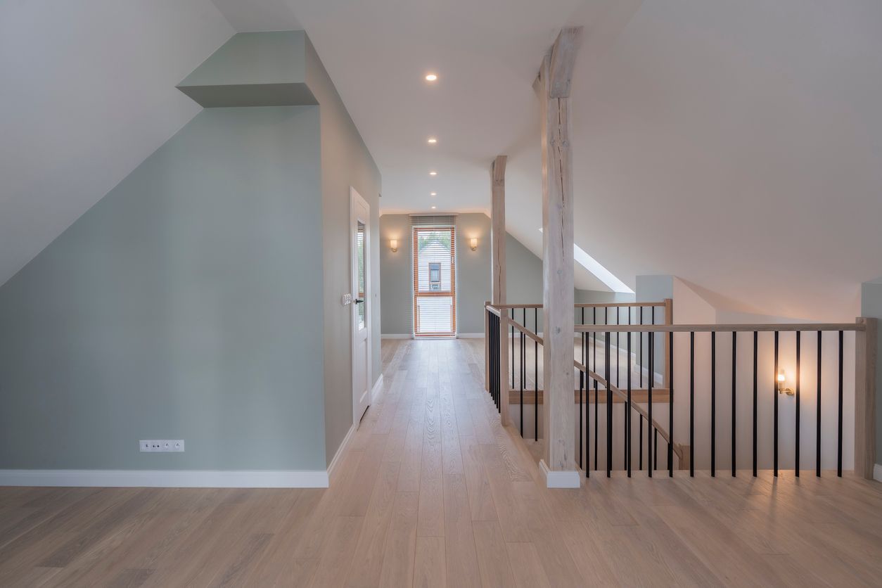 Bright upstairs hallway with light wood floors, pale walls, recessed lights, and a staircase railing on the right.