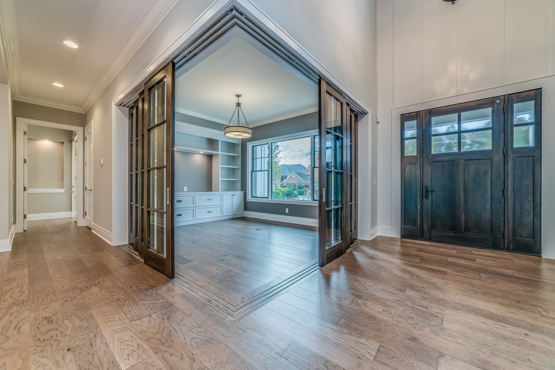 Open double doors to a bright kitchen with hardwood floors and dark front entry doors nearby