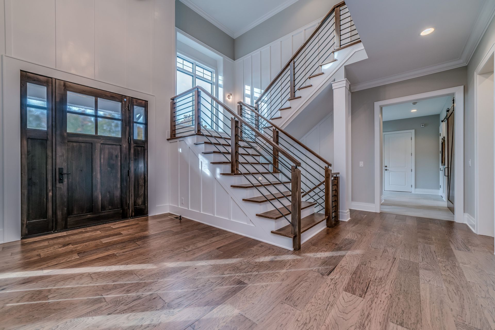 Bright foyer with hardwood floors, staircase, black double doors, and white walls