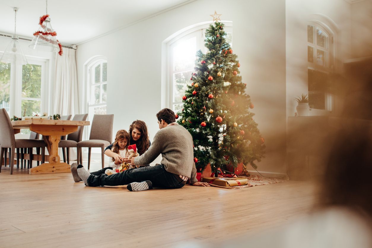 Family opening Christmas presents beside decorated tree.