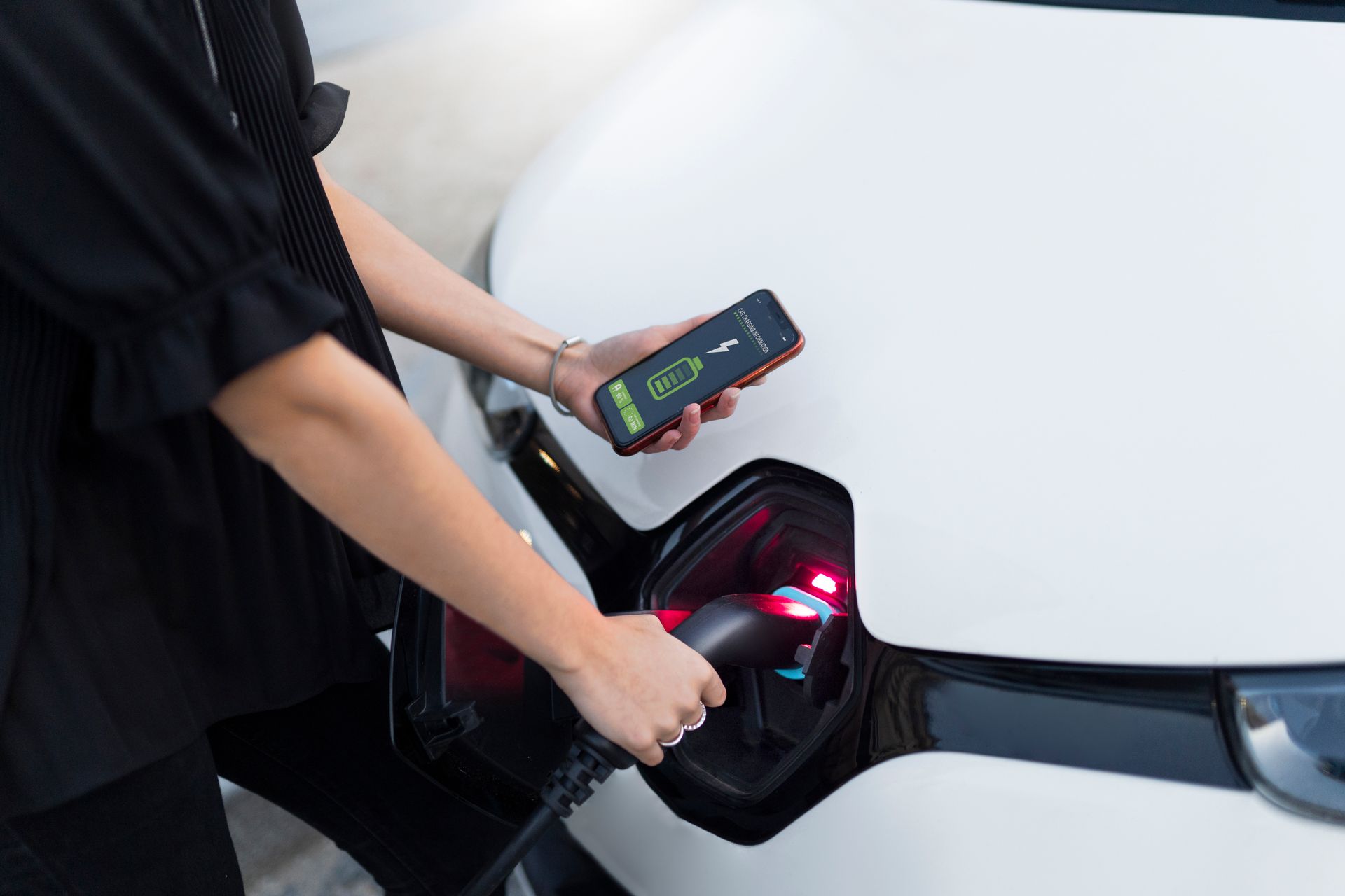 Une femme charge sa voiture électrique tout en tenant un téléphone portable.