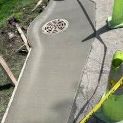 Newly poured concrete walkway with drain and safety cones.