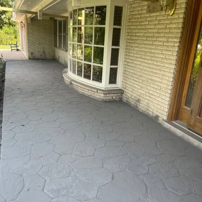 Gray concrete walkway with stone pattern, brick exterior, and a large bay window. Gray concrete walkway with stone pattern, brick exterior, and a large bay window.