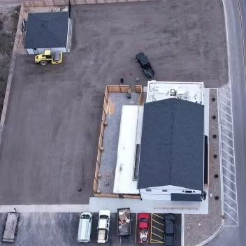Aerial view of a building with a dark roof and a parking lot with several vehicles.