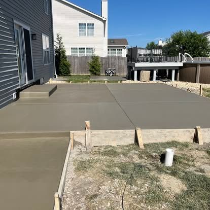 Newly poured concrete patio and walkway in a backyard, with wooden forms still in place.