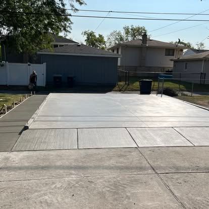 Newly poured concrete patio and walkway in a backyard, with a person nearby and surrounding houses.