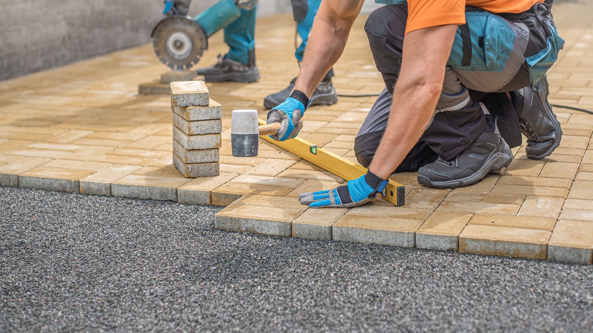 Concrete driveway installation crew leveling paving stones for residential outdoor surface. Concrete driveway installation crew leveling paving stones for residential outdoor surface.