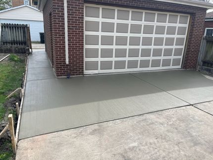 Freshly poured concrete driveway leading to a brick garage with a patterned door.