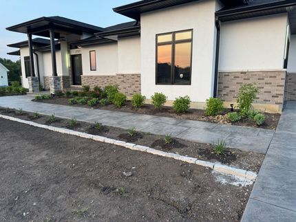 Modern house with landscaped beds, concrete walkway, and evening sky reflected in windows.