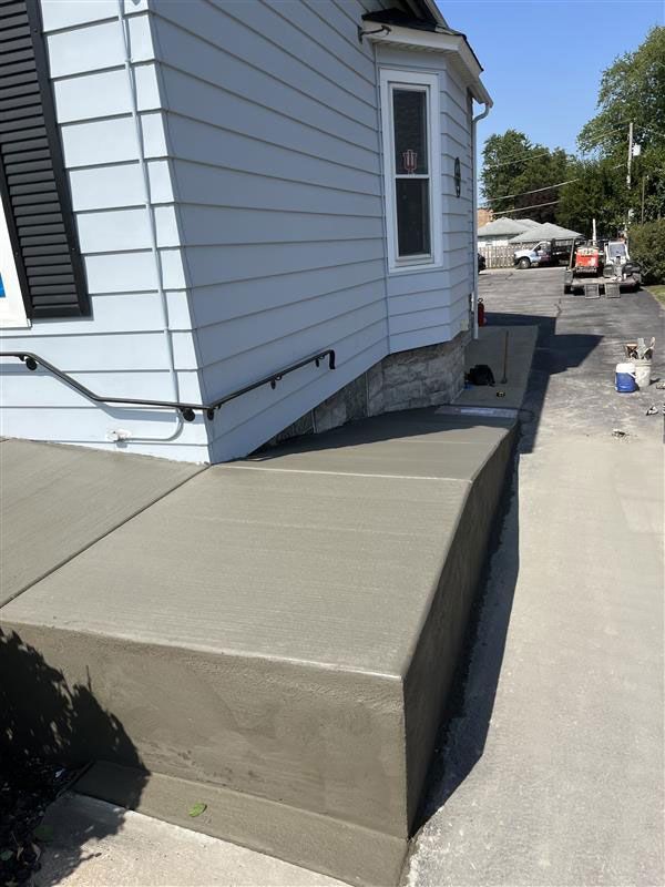 Newly poured concrete steps and walkway next to a light blue house.