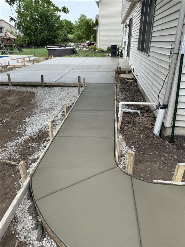 Newly poured concrete walkway and patio with wooden forms, next to a white house.