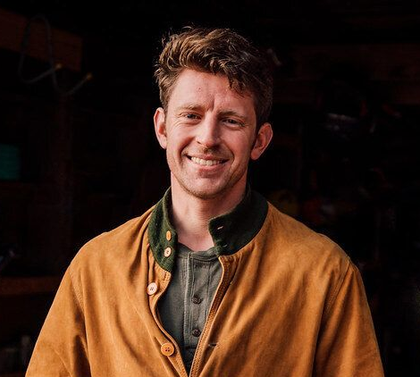 Man in an orange coat is smiling at the camera.