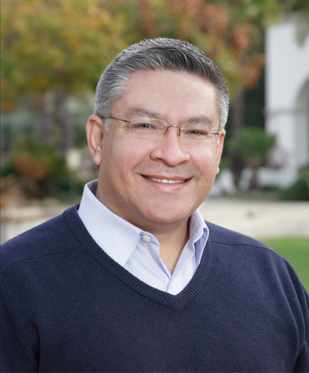 A man wearing glasses and a blue sweater smiles for the camera