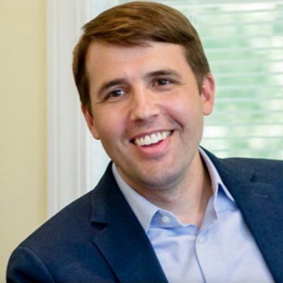 A man in a suit is smiling for the camera while sitting in front of a window.