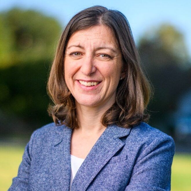 Woman in a blue suit jacket is smiling at the camera.