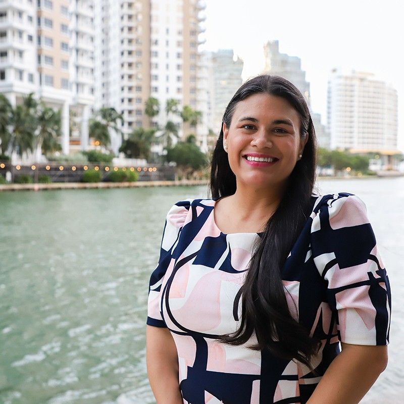 A woman in a pink and blue dress is smiling in front of a body of water