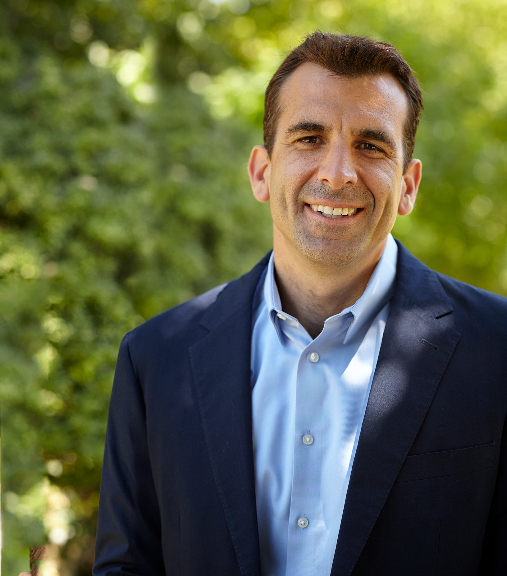 A man in a suit and blue shirt is smiling for the camera