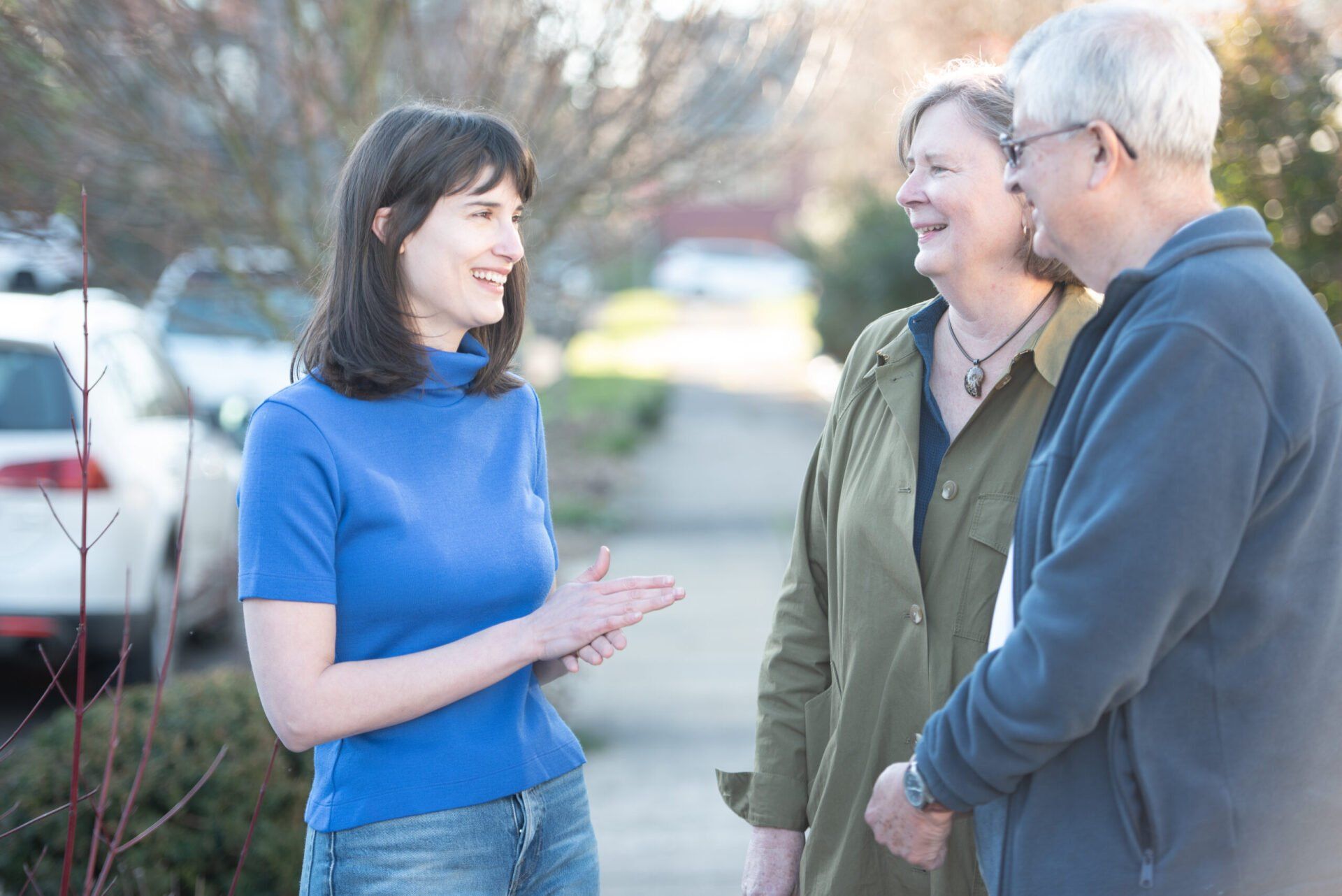 A woman in a blue shirt is talking to two people on a sidewalk.