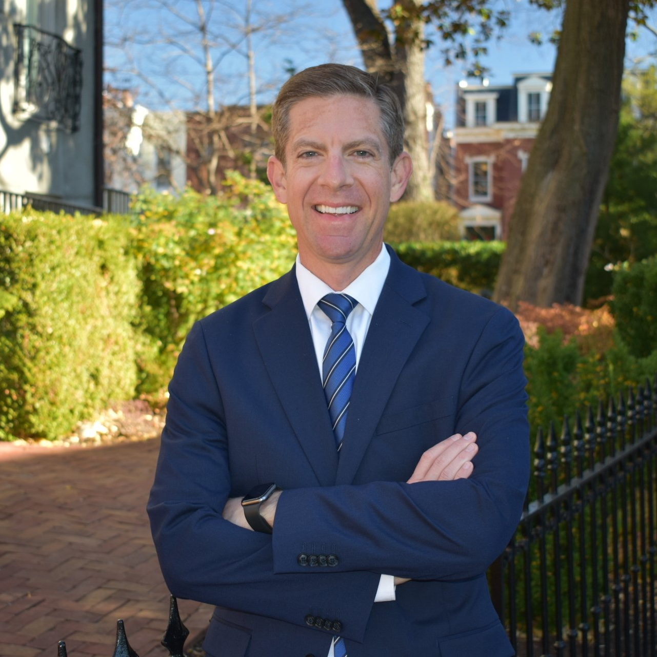 A man in a suit and tie is standing with his arms crossed and smiling.