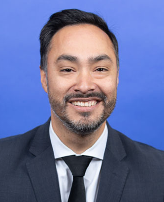 A man in a suit and tie is smiling in front of a blue background.