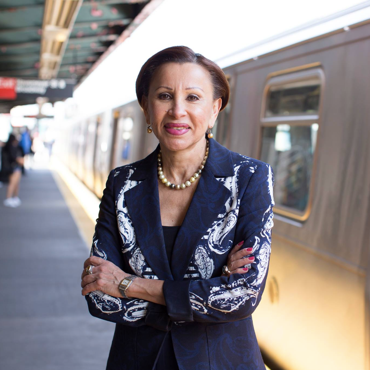 A woman in a blue jacket and pearls is standing in front of a train