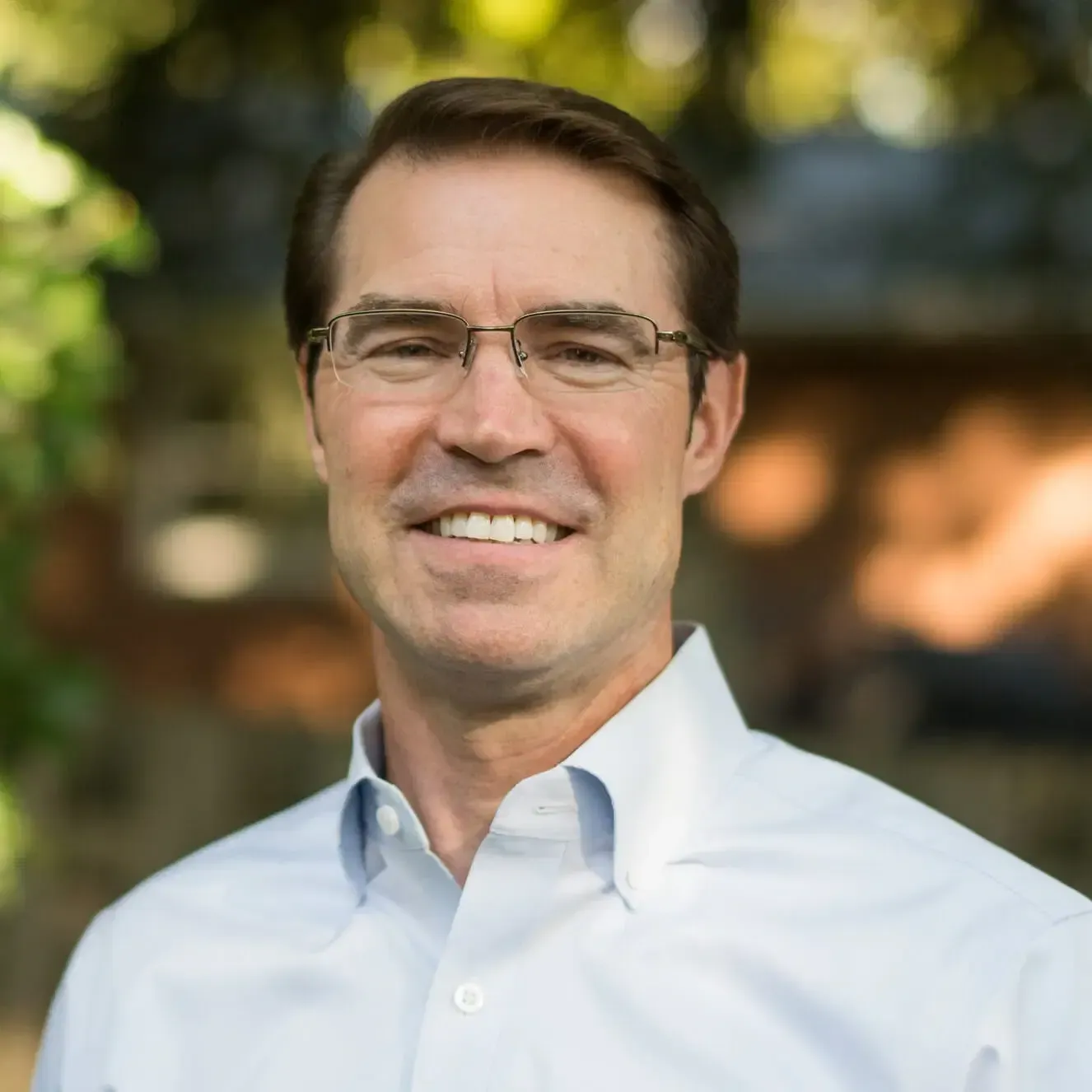 A man in a blue button down is smiling at the camera.