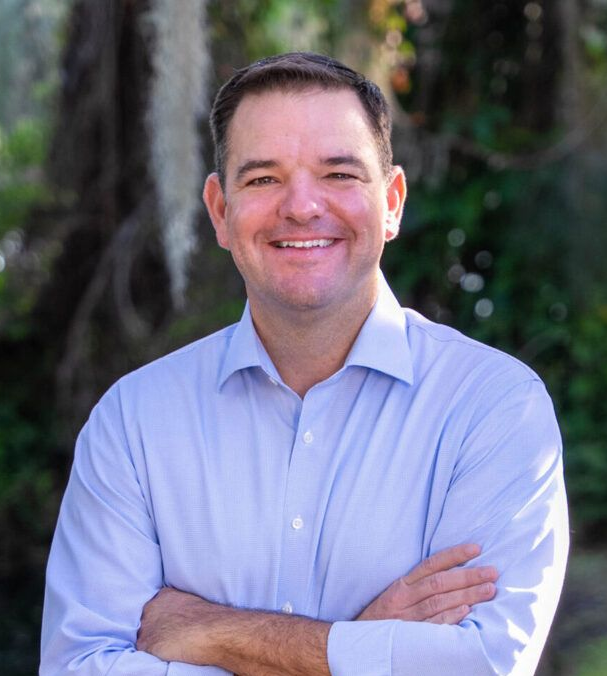 Man in a blue button down is smiling at the camera.