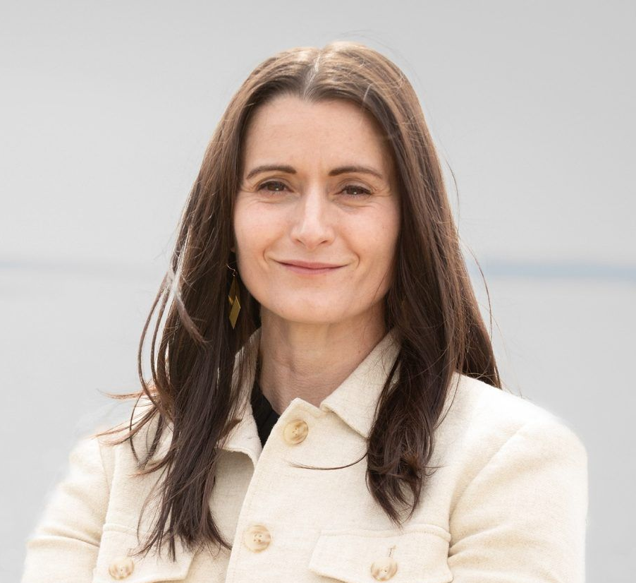 Woman in a white suit jacket is smiling at the camera.