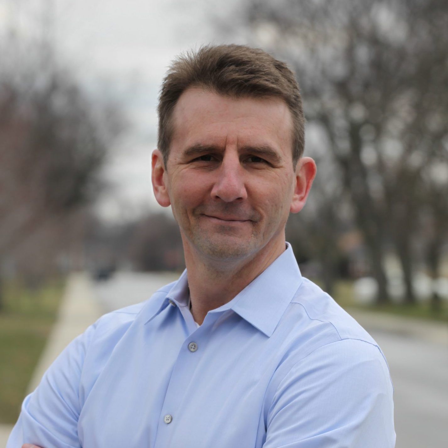 Man in a blue button down is smiling at the camera.