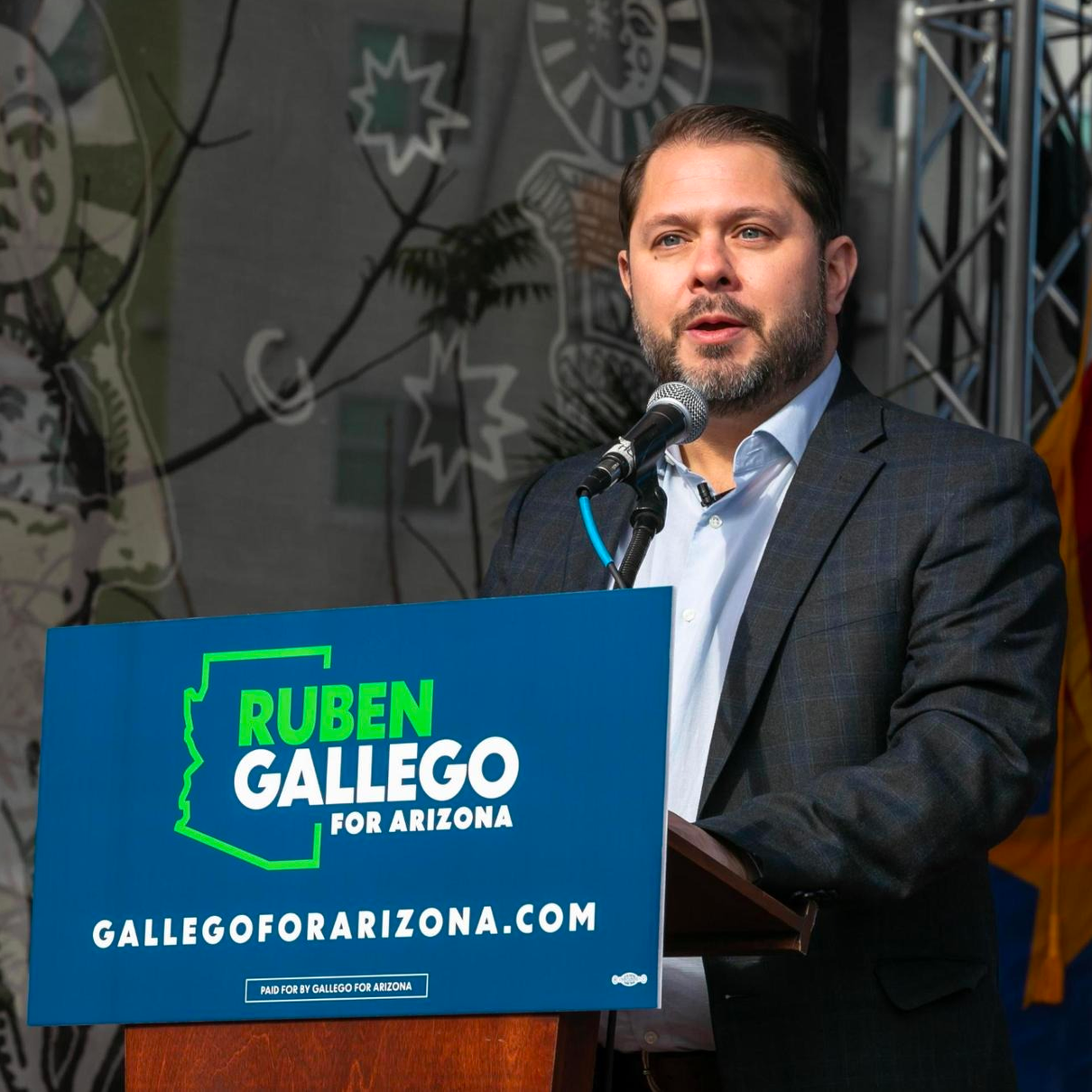 A man stands at a podium with a sign that says ruben gallego for arizona