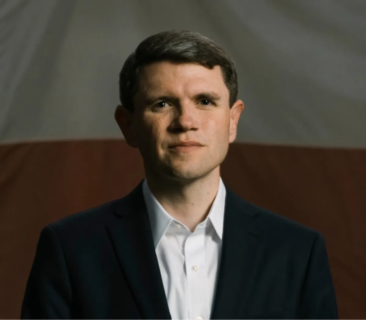 A man in a blue suit is looking straight at the camera.