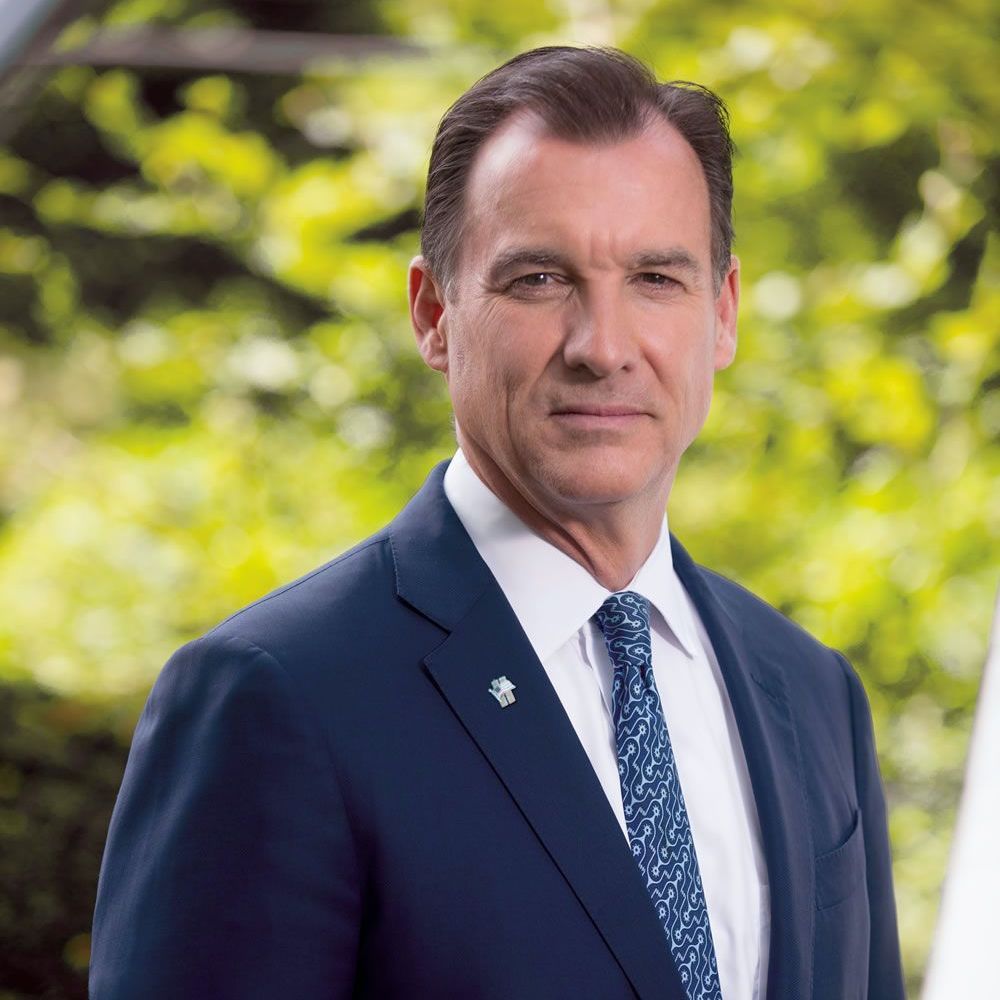 A man in a suit and tie is standing in front of trees