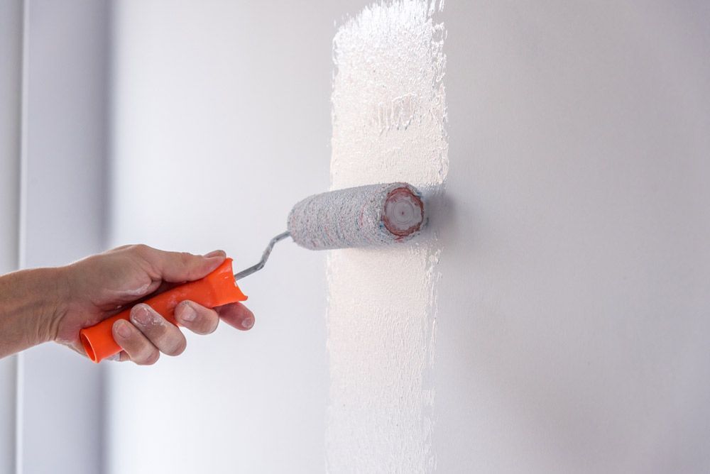 Painter Painting A House Wall With A Paint Roller — Building Supplies in Narrabri, NSW