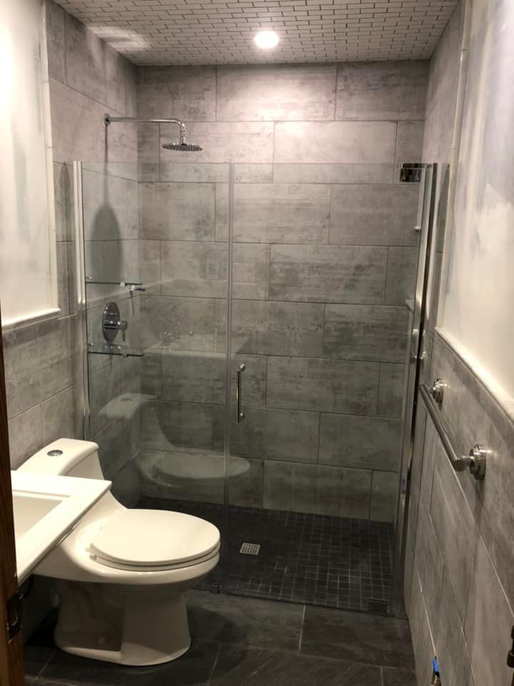 Small bathroom with glass shower, gray tile walls, and a white toilet.