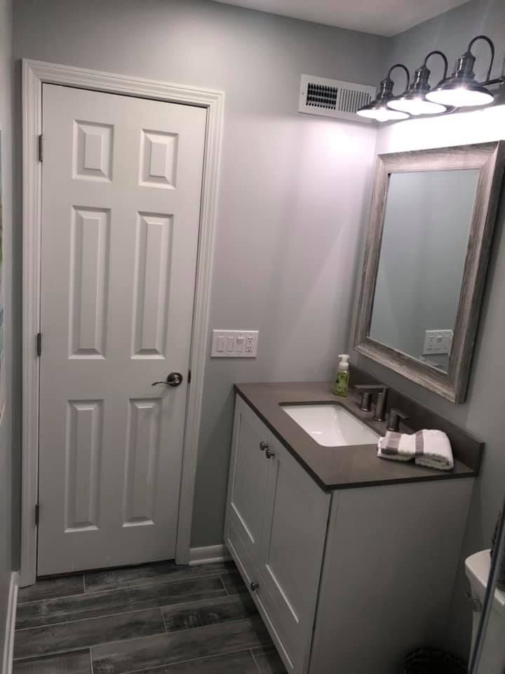 Bathroom with white door, vanity, mirror, and gray walls and floor.