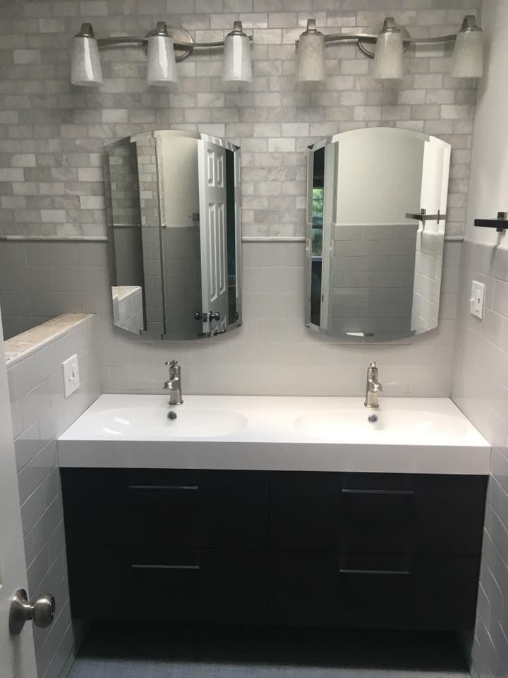 Bathroom with dual sinks, mirrors, and dark cabinet. Gray and white color scheme, overhead lighting.