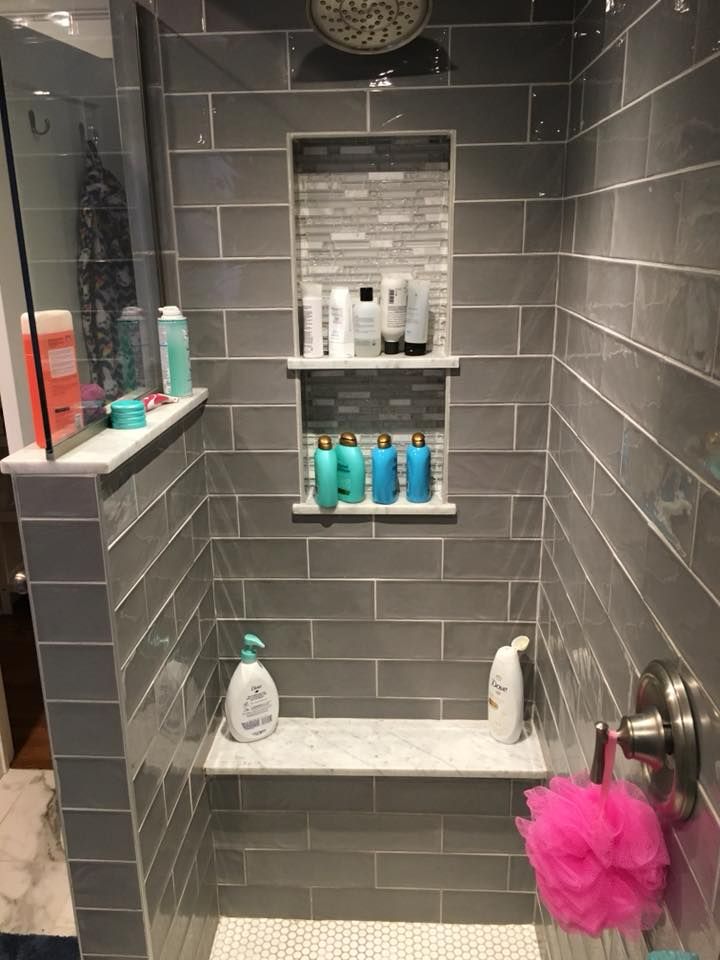 Gray tiled shower with built-in shelves holding toiletries. Pink loofah hangs from the faucet.