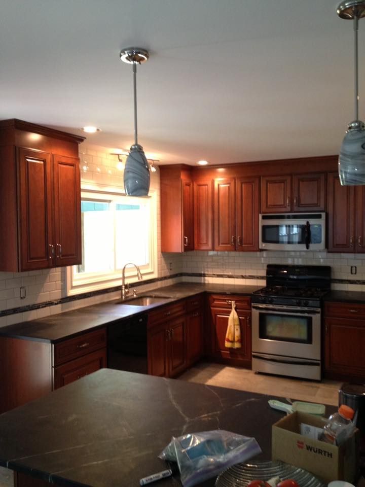 Cherry-wood kitchen with stainless steel appliances, dark countertops, and pendant lights.