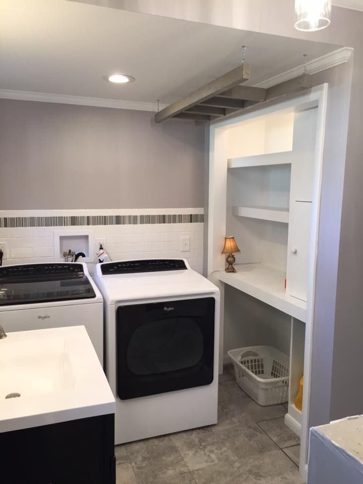 Laundry room with washer, dryer, built-in desk, and shelving. Gray walls, white trim and appliances.