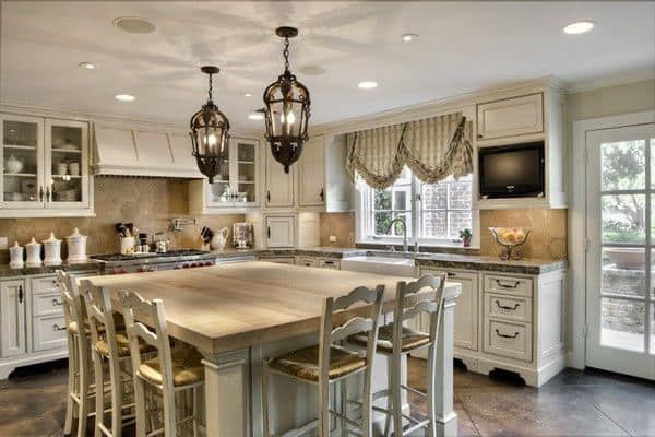 Elegant kitchen with large island, hanging lanterns, and glass-front cabinets. Pale wood and cream tones.