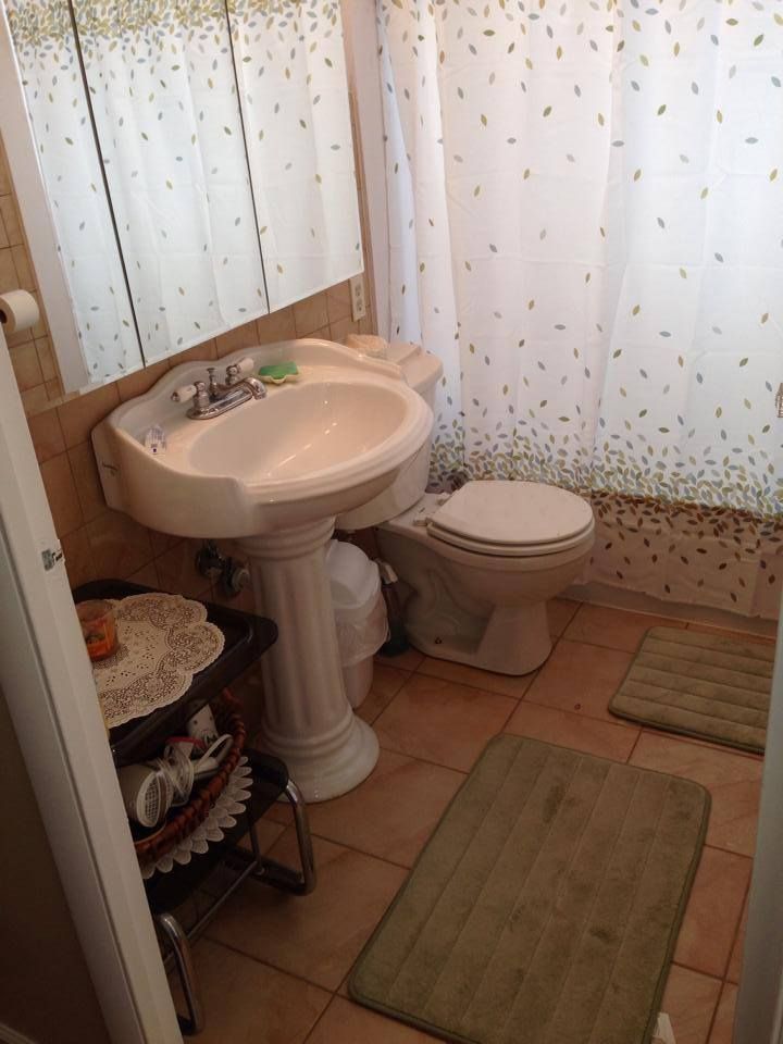 Bathroom with pedestal sink, toilet, beige tiled floor, and leaf patterned shower curtain.